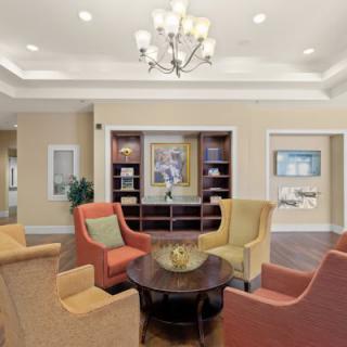 A modern lobby seating area with colorful chairs, a central table, and a chandelier overhead.