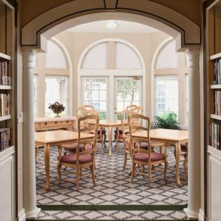 A bright dining room with arched windows, wooden tables and chairs, and a patterned tile floor.