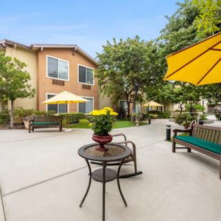 A peaceful outdoor patio area with tables, benches, and umbrellas next to an apartment building.