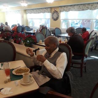 An elderly man enjoying a meal in a cozy dining area with others around.