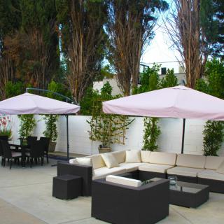 A stylish outdoor patio featuring comfortable seating with umbrellas set against a backdrop of tall trees.