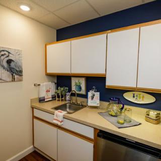 A small kitchen setup with white cabinets, a blue accent wall, and countertop items including a beverage pitcher and cups.