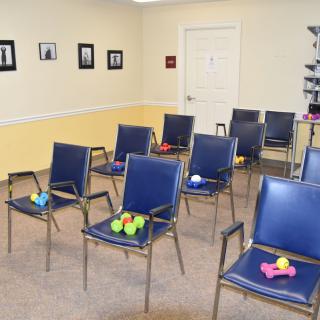 An indoor waiting room setup featuring blue chairs, each holding small exercise equipment like dumbbells and balls.