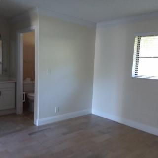 An empty room with hardwood floors, a window, and an open doorway leading to a bathroom.