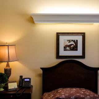 A cozy bedroom corner featuring a bedside lamp, wall art, and soft lighting.