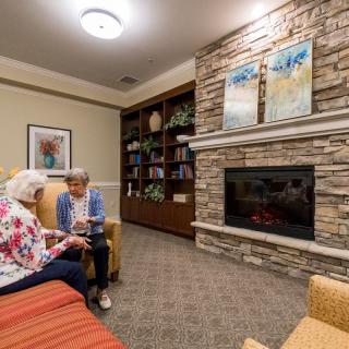 Two people engaged in conversation in a cozy living room with a fireplace.