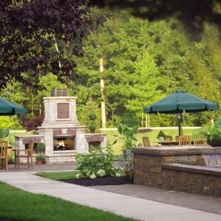 A serene outdoor garden patio with tables, chairs, and umbrellas amidst lush greenery.
