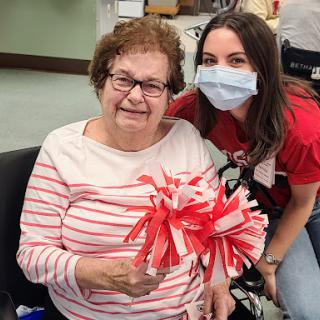 A joyous moment shared between a caregiver and an elderly woman, celebrating with colorful pom-poms.