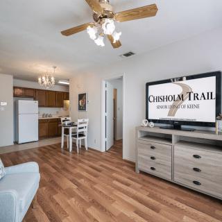 A cozy apartment interior featuring a living room with wood flooring, a ceiling fan, and an open kitchen and dining area.