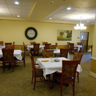A cozy dining room with neatly arranged tables and chairs, adorned with a large wall clock and artwork.