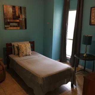 A cozy bedroom with blue walls, featuring a single bed, decorative pillows, and a nightstand with a lamp.