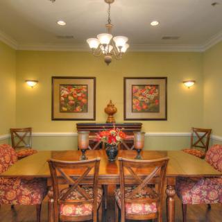 A cozy dining room with a wooden table and floral-patterned chairs, illuminated by a chandelier and decorated with wall art.