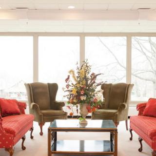A cozy living room with comfortable seating arrangements, featuring two sofas and armchairs around a glass coffee table with a floral centerpiece.