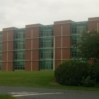 A modern brick building with large windows surrounded by grass and shrubs.