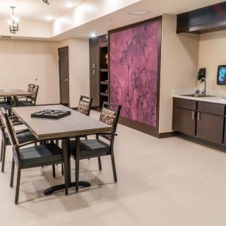 A modern dining area with tables and chairs, featuring a kitchenette and colorful wall art.
