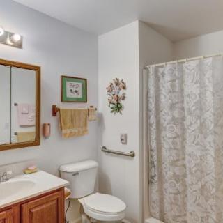 A clean and organized bathroom with a toilet, sink, mirror, and shower area.