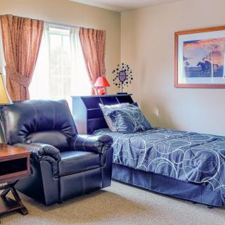 A cozy bedroom with a single bed and an armchair next to a window with curtains.