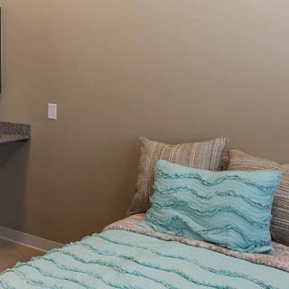 A cozy bedroom with a neatly made bed featuring blue patterned bedding and pillows against a beige wall.