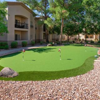 A landscaped apartment courtyard with a putting green surrounded by rocks and trees on a sunny day.