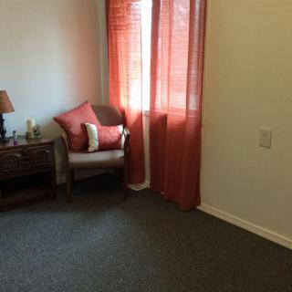 A cozy room with a chair next to a window dressed in red curtains, complemented by a small lamp on an end table.