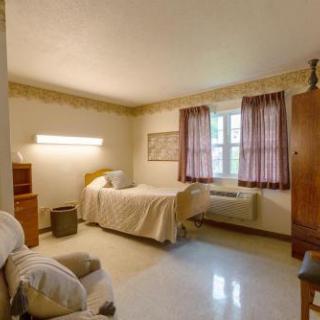 A cozy and simple bedroom featuring a single bed, a comfortable chair, and soft curtains.