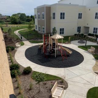 A small playground with a slide located in an apartment complex courtyard, surrounded by landscaped paths.