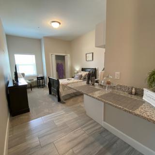A cozy studio apartment featuring a small kitchenette and a comfortable sleeping area, illuminated by natural light.