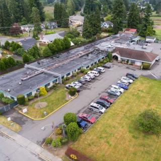 Aerial view of a building with an adjacent parking lot in a suburban area surrounded by trees.