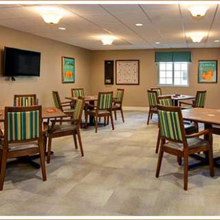 A well-lit community room with several tables and chairs, featuring a television and a window.