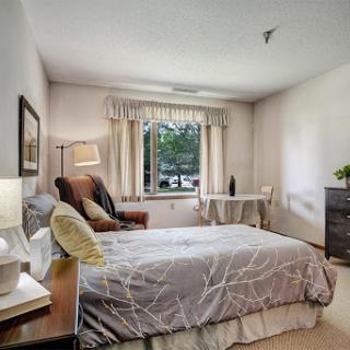 A cozy and well-lit bedroom featuring a neatly made bed, soft furnishings, and a warm atmosphere.