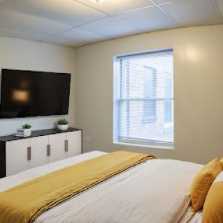 A cozy and modern bedroom featuring a stylish bed, television, and ample natural light.