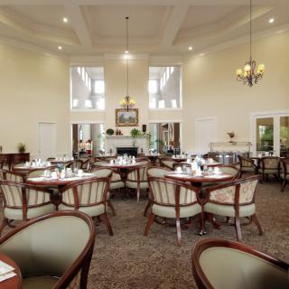 A spacious dining area with elegant tables and chairs, a chandelier, and large windows.