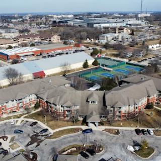 Aerial view of a residential complex surrounded by commercial establishments and tennis courts.
