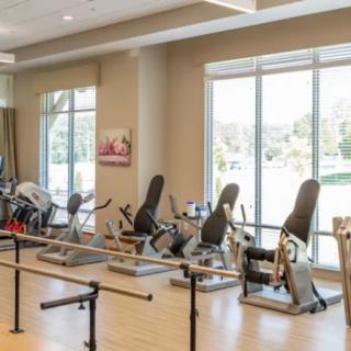 A physical therapy room with various exercise equipment and large windows.