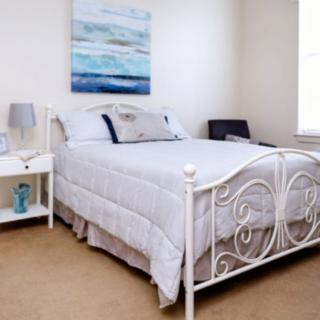 A cozy bedroom with a white metal bed frame, soft white bedding, and a nightstand with a lamp.