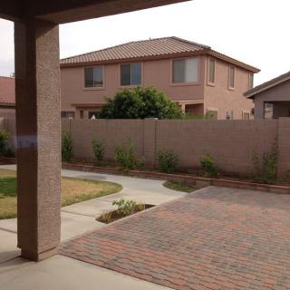 A suburban backyard with a paved area, lawn, and surrounding fence.