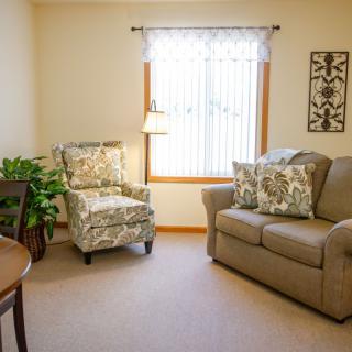 A cozy living room with a beige couch, floral armchair, and natural light from a window.