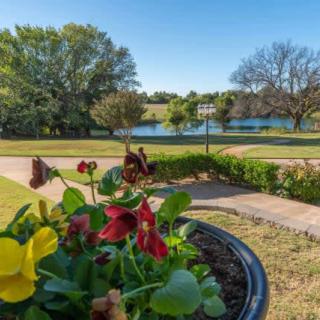 A scenic view of a garden with colorful flowers in the foreground, a lake, and lush trees in the background.
