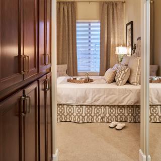 A cozy bedroom with elegant decor, featuring a well-made bed, soft lighting from a lamp, and neatly arranged pillows.