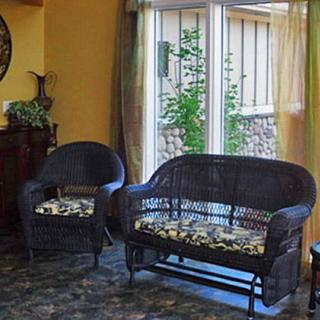 A cozy living room with wicker furniture and a view of the garden through a large window.