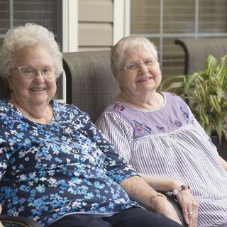 Two elderly women sitting together on a patio, smiling and enjoying the outdoors.