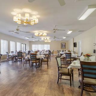 A spacious dining room with neatly arranged tables and chairs, featuring large windows and elegant chandeliers.
