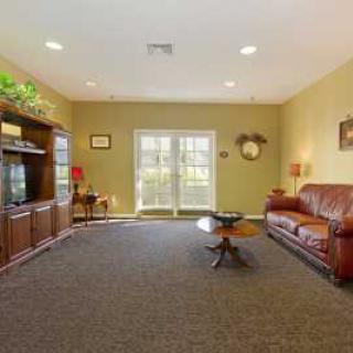 A spacious living room with a brown leather sofa, a coffee table, and an entertainment center, featuring large windows and warm lighting.