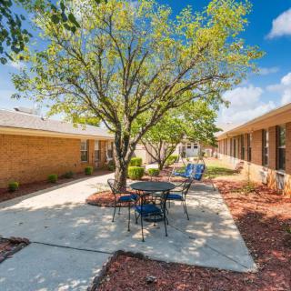 A sunny courtyard with outdoor seating and a tree between two buildings.