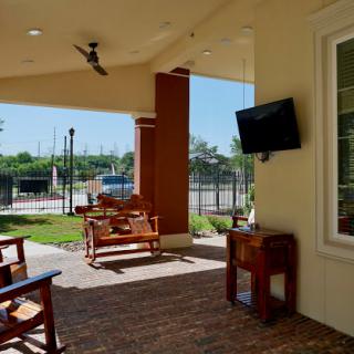 A cozy outdoor patio space featuring wooden rocking chairs and a television, surrounded by greenery.