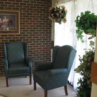 A cozy seating area featuring two upholstered chairs and decorative plants against a brick wall.