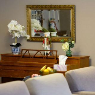 A cozy living room featuring a piano adorned with elegant flower arrangements and a decorative mirror above.