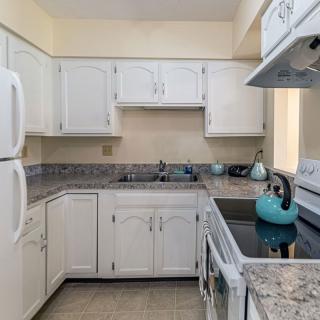 A cozy kitchen with white cabinets, granite countertops, and a turquoise teapot on the stove.
