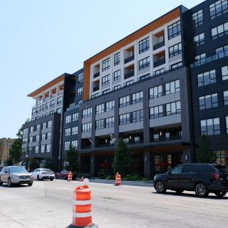 A modern apartment building with cars on the street and construction cones nearby.