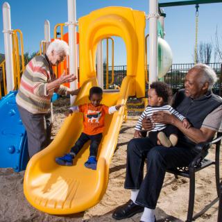 A joyful moment at the playground with children on the slide and grandparents watching.